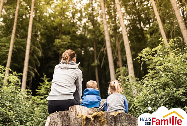 Frau und zwei Kinder sitzen auf Baumstamm in der Natur