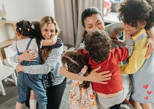 2 Frauen umarmen mehrere Kinder