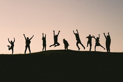 Silouetten von 8 Personen auf einem H&uuml;gel, die die Arme in die H&ouml;he strecken und unterschiedliche Bewegungen ausf&uuml;hren.