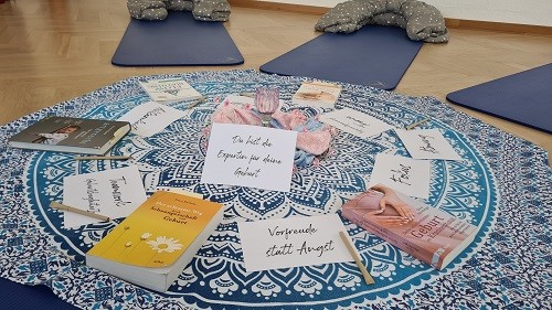 Sitzkreis auf Yogamatten um eine runde Decke. Darauf B&uuml;cher und Karten mit positiven Botschaften rund um Schwangerschaft und Geburt.