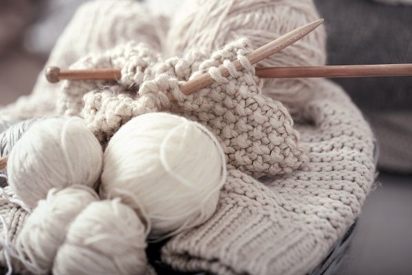 wei&szlig;e teils gestrickte Wolle mit Stricknadeln aus Holz