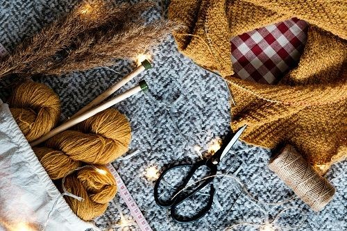 Wolle, Schere, Garn, Ma&szlig;band, Stricknadeln eine leuchtende Lichterkette und ein fast fertiges gestricktes Tuch auf einer grauen Decke