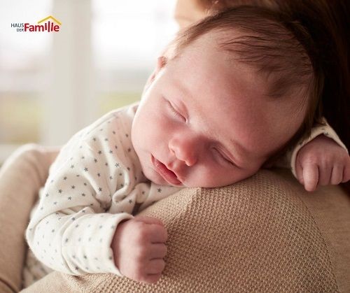 Ein schlafendes Baby liegt &uuml;ber der Schulter einer erwachsenen Person.