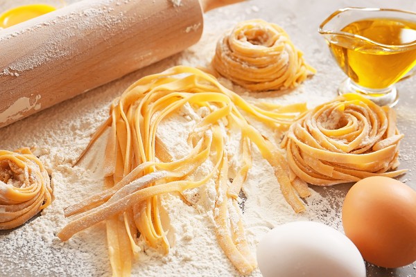 Handgemachte Pasta roh, daneben ein Nudelholz, ein Ei und &Ouml;l