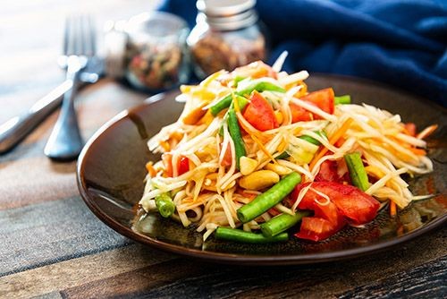 Thail&auml;ndischer Papaya Salat auf dunkelbraunem Teller.