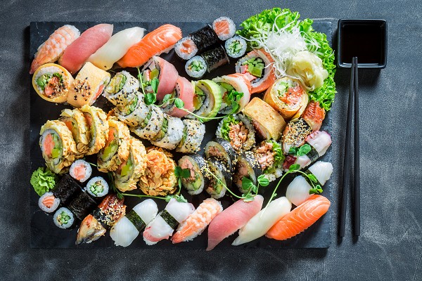 Eine gro&szlig;e Auswahl an verschiedenem Sushi auf einer schwarzen Schieferplatte aus der Vogelperspektive.