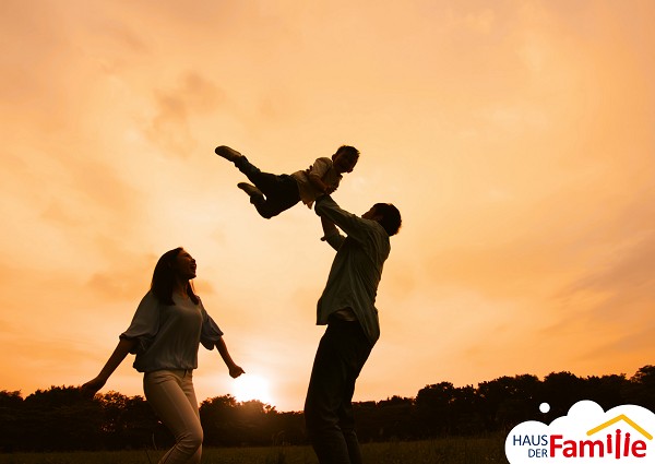 Eine Familie ist drau&szlig;en am spielen. Der Vater wirft sei Kind im Arm in die Luft.
