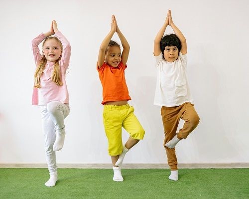 3 Kinder machen die Yoga &Uuml;bung der Baum. Die H&auml;nde sind &uuml;ber dem Kopf zusammengebracht und ein Bein wird angewinkelt