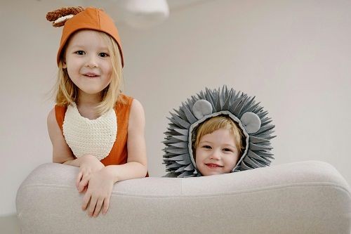 2 Kinder hocken auf dem Sofa und schauen &uuml;ber die Sofalehne. Sie sind als Tiere verkleidet. Eines ist wahrscheinlich ein Fuchs und das andere ein grauer B&auml;r mit M&auml;hne.