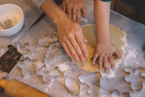 Ausstechformen liegen nebeneinander, Kinder und Erwachsenenh&auml;nde stechen Teig aus