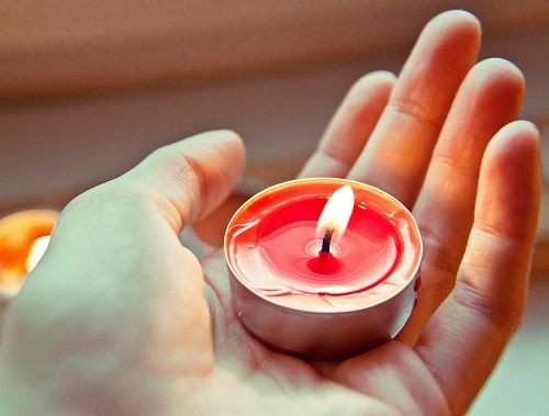 eine Hand h&auml;lt ein rotes leuchtendes Teelicht