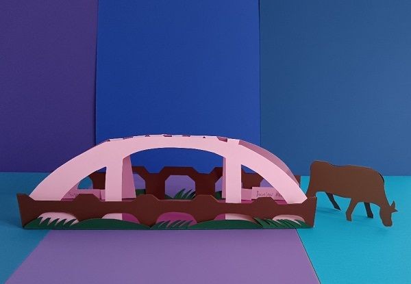 eine Br&uuml;cke vor blauem Hintergrund mit einer Kuh am rechten Ende der Br&uuml;cke aus Pappe gefaltet