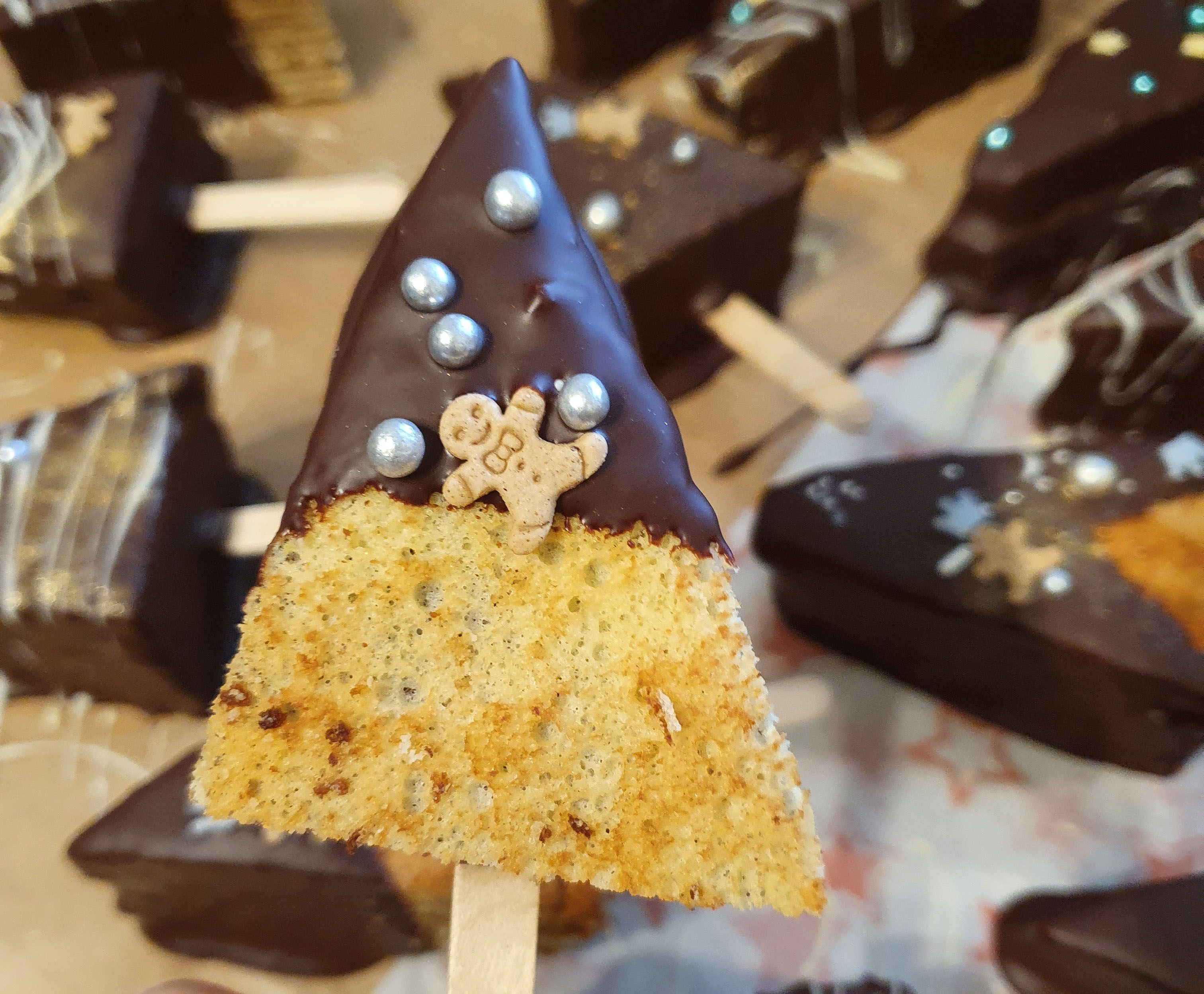 Eine Baumkuchenspitze am Stiel, verziert mit Schokolade, silbernen Perlen und einem Mini-Lebkuchen-Keks