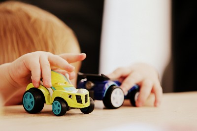 Kleinkind spielt auf Augenh&ouml;he mit 2 Spielzeugautos auf dem Tisch.